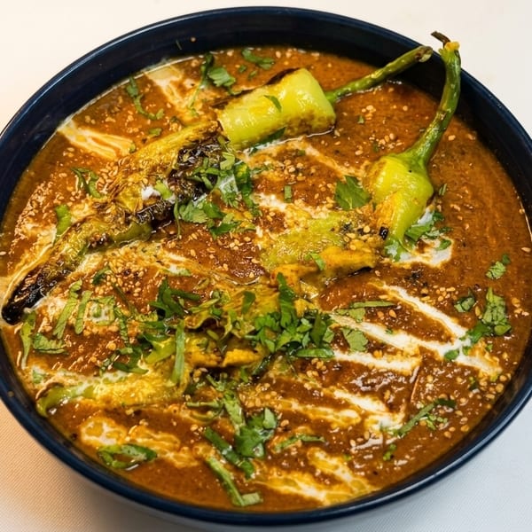 A dark blue bowl filled with a rich brown curry, garnished with green peppers, cream, and cilantro.