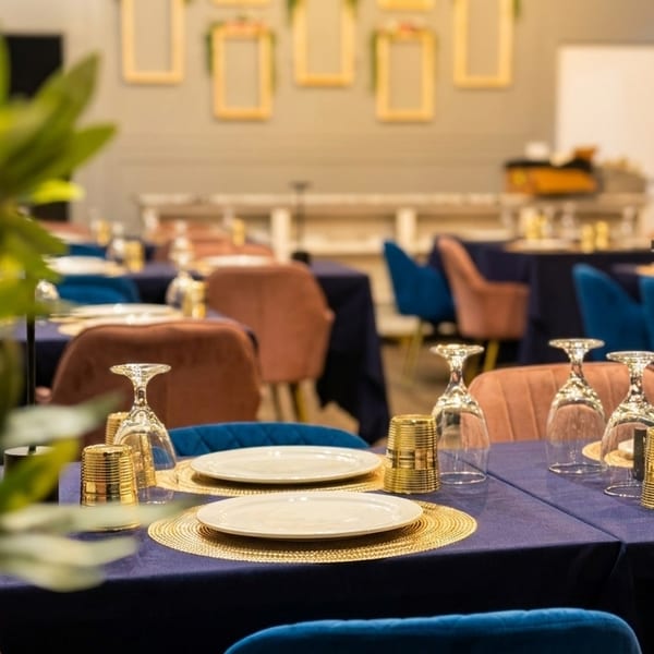 Restaurant dining room with blue and brown chairs, set tables with blue tablecloths, and gold accents.
