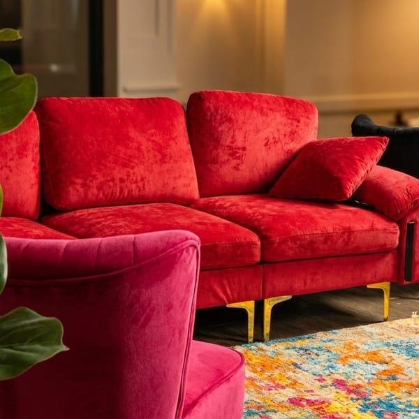 Vibrant red velvet sofa and pink armchair with a colorful rug in a cozy lounge area.