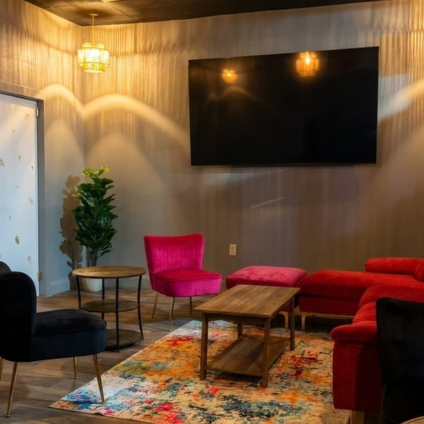 Lounge area with red and pink seating, a colorful rug, and a large TV on the wall.